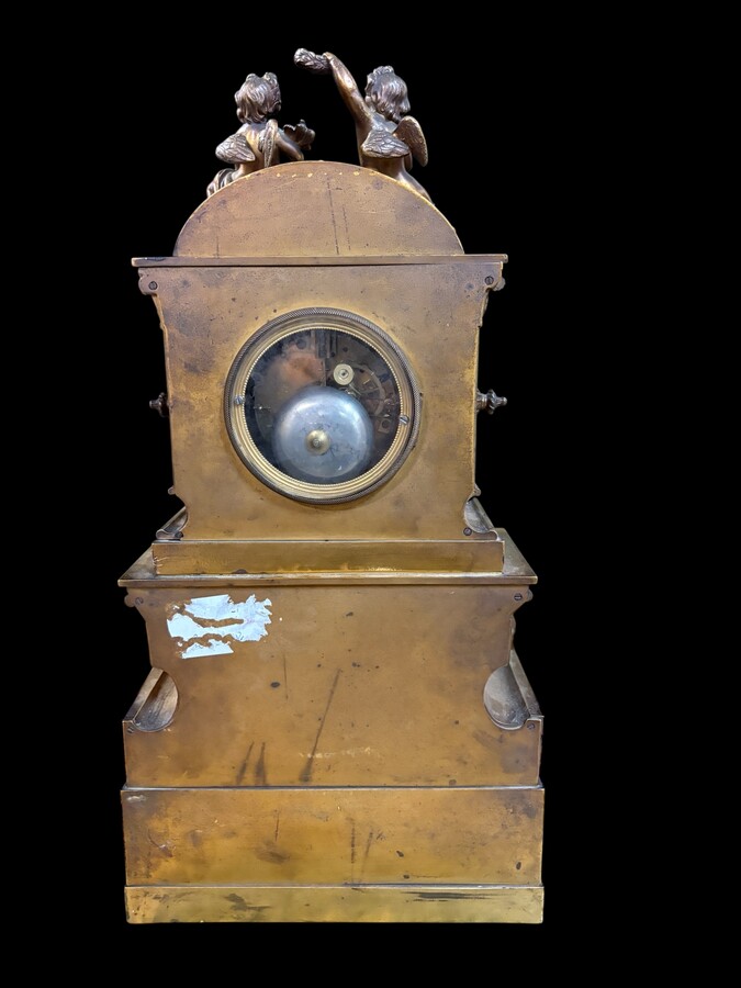 Romantic Napoleon III-style bronze mantelpiece set A mantelpiece set comprising a clock adorned with angels, figures, decorative motifs and a building with a staircase, as well as a pair of candlesticks richly decorated with mythological creatures. 