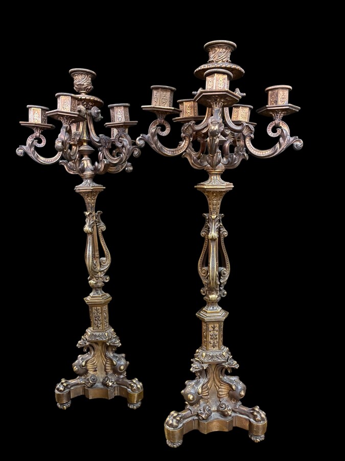 Romantic Napoleon III-style bronze mantelpiece set A mantelpiece set comprising a clock adorned with angels, figures, decorative motifs and a building with a staircase, as well as a pair of candlesticks richly decorated with mythological creatures. 