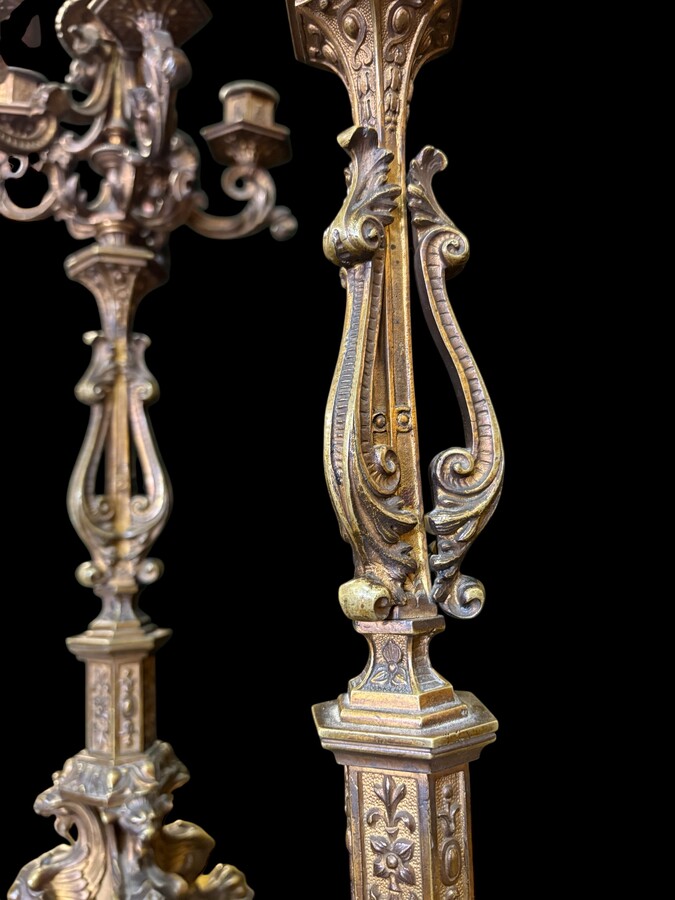 Romantic Napoleon III-style bronze mantelpiece set A mantelpiece set comprising a clock adorned with angels, figures, decorative motifs and a building with a staircase, as well as a pair of candlesticks richly decorated with mythological creatures. 