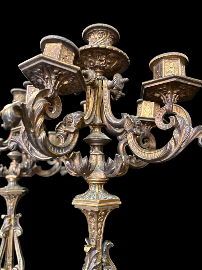 Romantic Napoleon III-style bronze mantelpiece set A mantelpiece set comprising a clock adorned with angels, figures, decorative motifs and a building with a staircase, as well as a pair of candlesticks richly decorated with mythological creatures. 