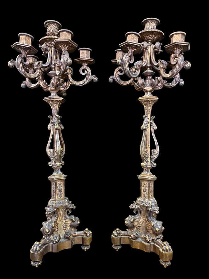 Romantic Napoleon III-style bronze mantelpiece set A mantelpiece set comprising a clock adorned with angels, figures, decorative motifs and a building with a staircase, as well as a pair of candlesticks richly decorated with mythological creatures. 
