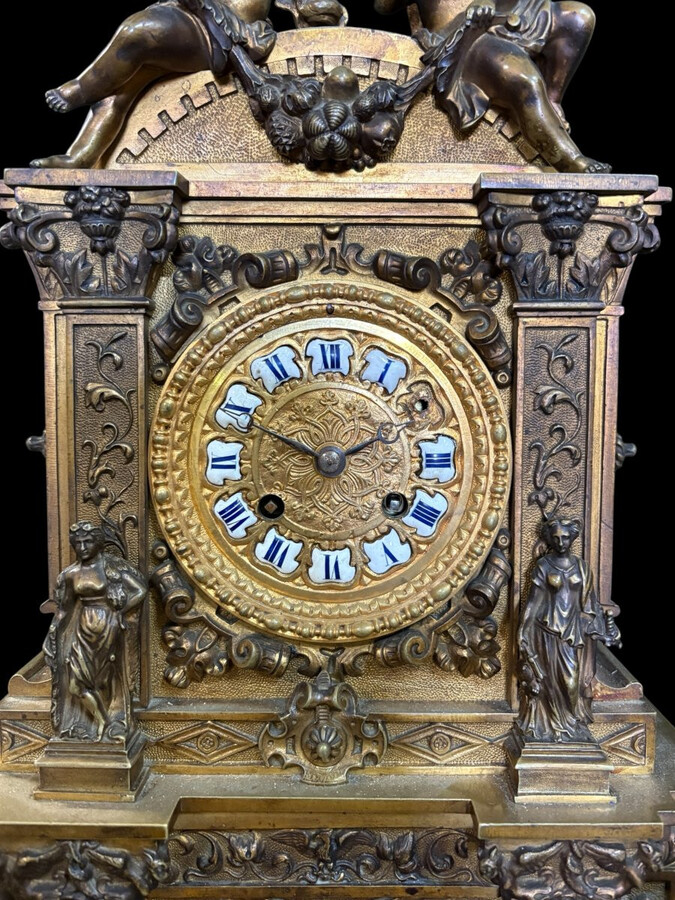 Romantic Napoleon III-style bronze mantelpiece set A mantelpiece set comprising a clock adorned with angels, figures, decorative motifs and a building with a staircase, pair of candlesticks richly decorated with mythological creatures.
