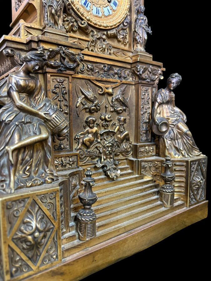 Romantic Napoleon III-style bronze mantelpiece set A mantelpiece set comprising a clock adorned with angels, figures, decorative motifs and a building with a staircase, pair of candlesticks richly decorated with mythological creatures.